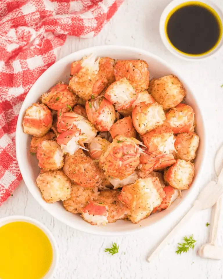 A white bowl filled with golden air fryer crab bites, surrounded by dipping sauces and a red checkered towel.