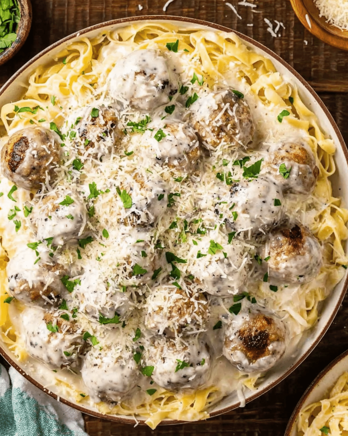 A bowl of Alfredo meatballs served over fettuccine pasta, topped with creamy Alfredo sauce, shredded Parmesan cheese, and fresh parsley.