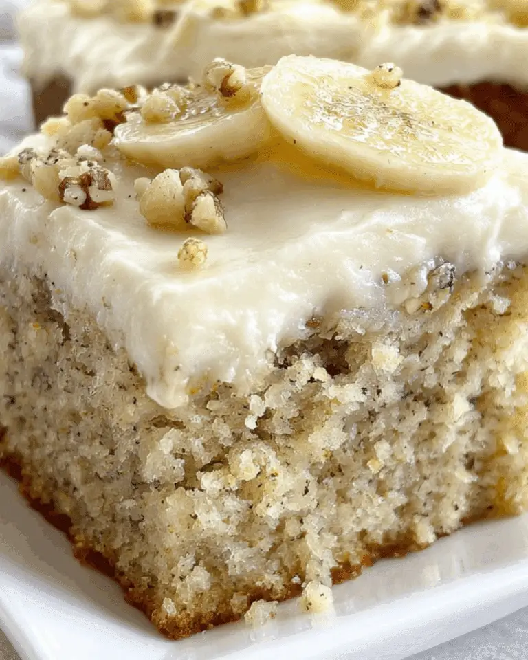Moist slice of Banana Bread Cake with Cream Cheese Frosting, topped with banana slices and chopped nuts on a white plate.