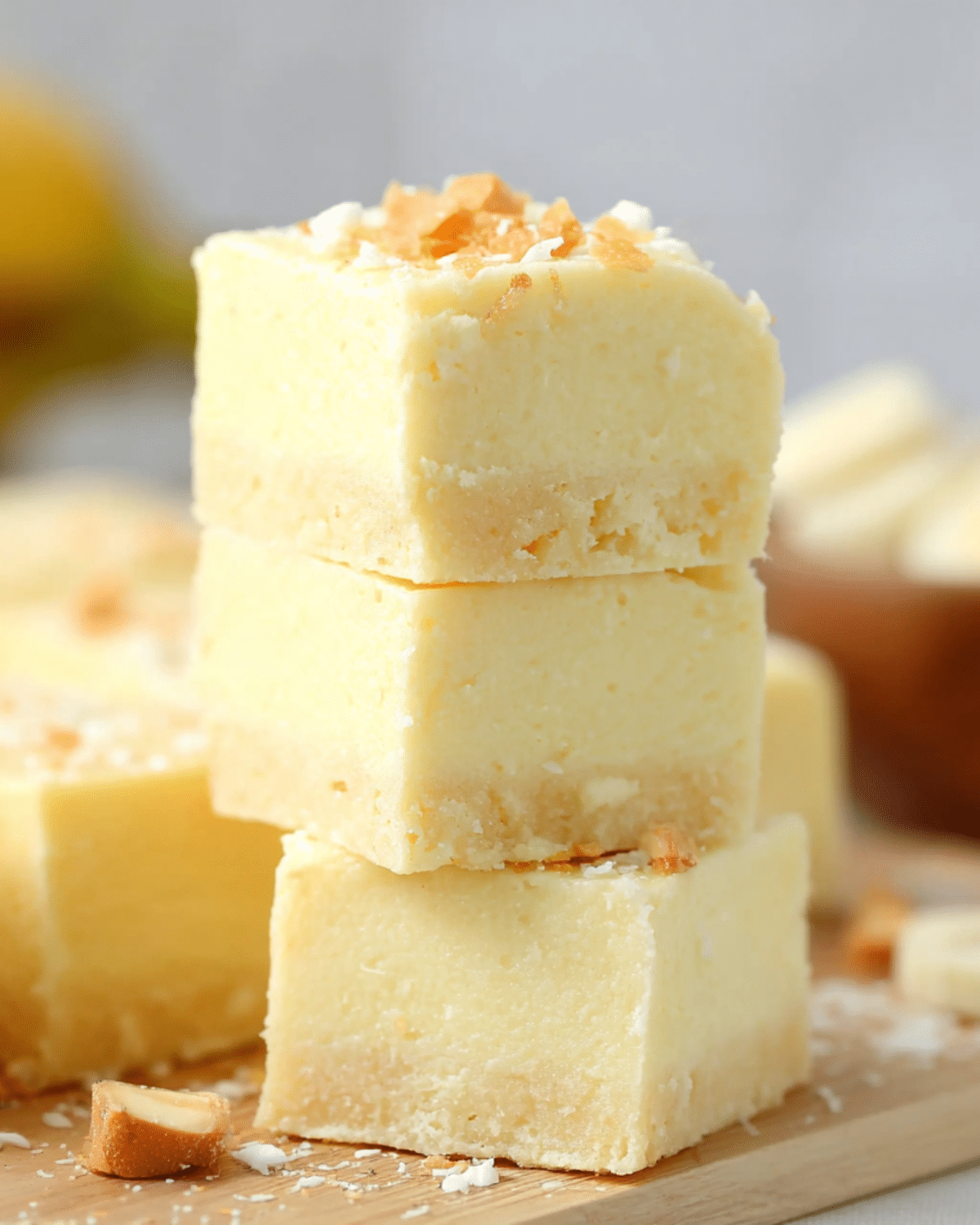 Stack of creamy banana fudge squares with a smooth texture, topped with shredded coconut and banana chips.