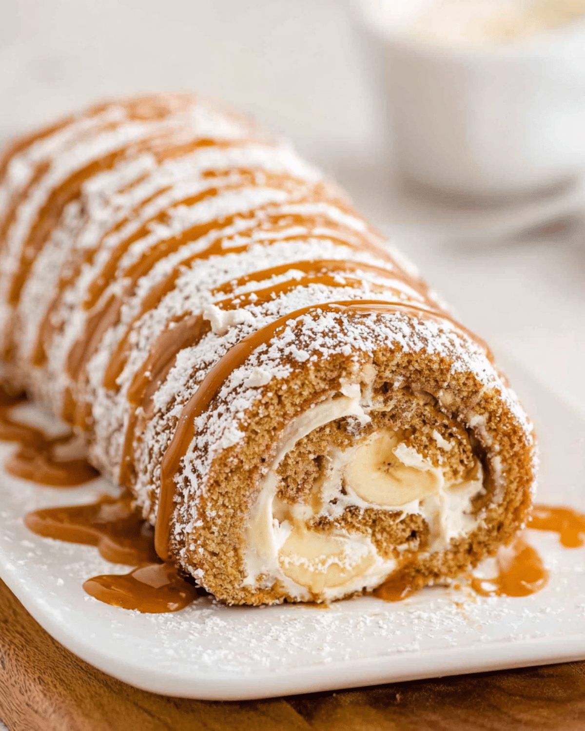 Banana roll cake filled with whipped cream and fresh banana slices, topped with powdered sugar and caramel drizzle.