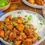 Plate of Bourbon Chicken Bites glazed in a rich sauce, served with white rice and garnished with chopped green onions.