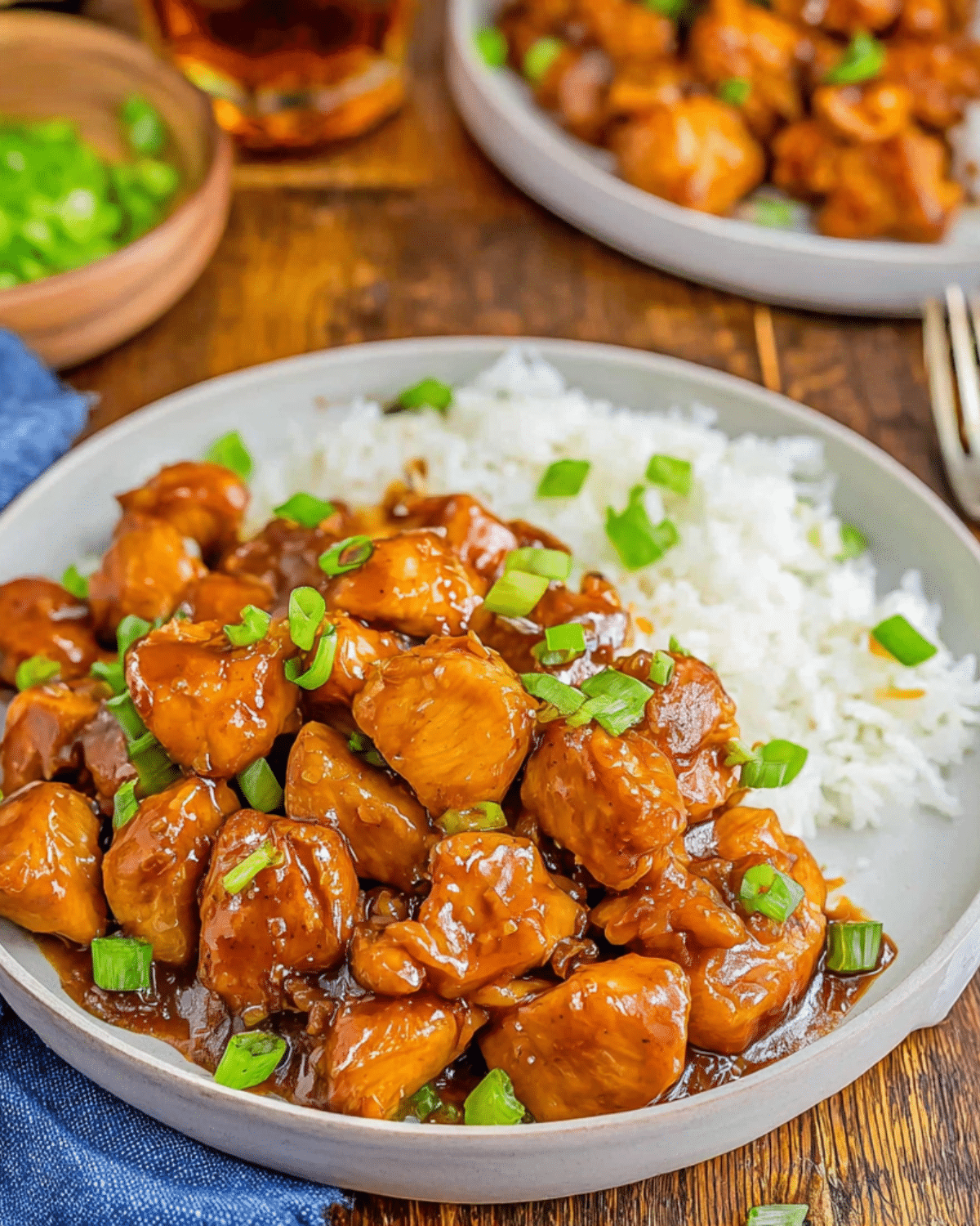 Plate of Bourbon Chicken Bites glazed in a rich sauce, served with white rice and garnished with chopped green onions.