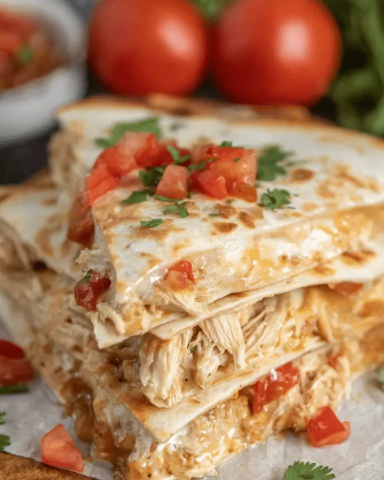 Stacked crockpot queso chicken quesadillas filled with shredded chicken, melted cheese, and topped with diced tomatoes and cilantro.