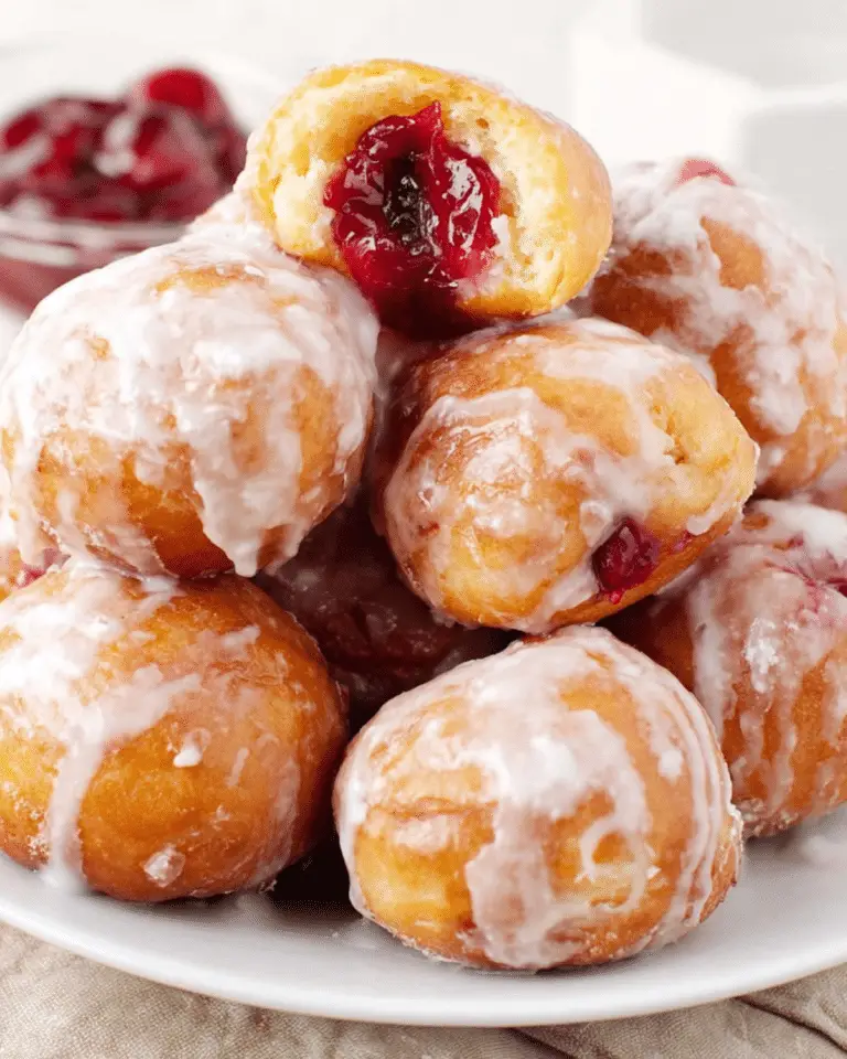 Glazed cherry pie bombs stacked on a white plate, with one cut open to reveal a cherry filling.