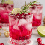 Cranberry Christmas Cocktail in a clear glass filled with ice, garnished with fresh cranberries, a lime slice, and a sprig of rosemary.