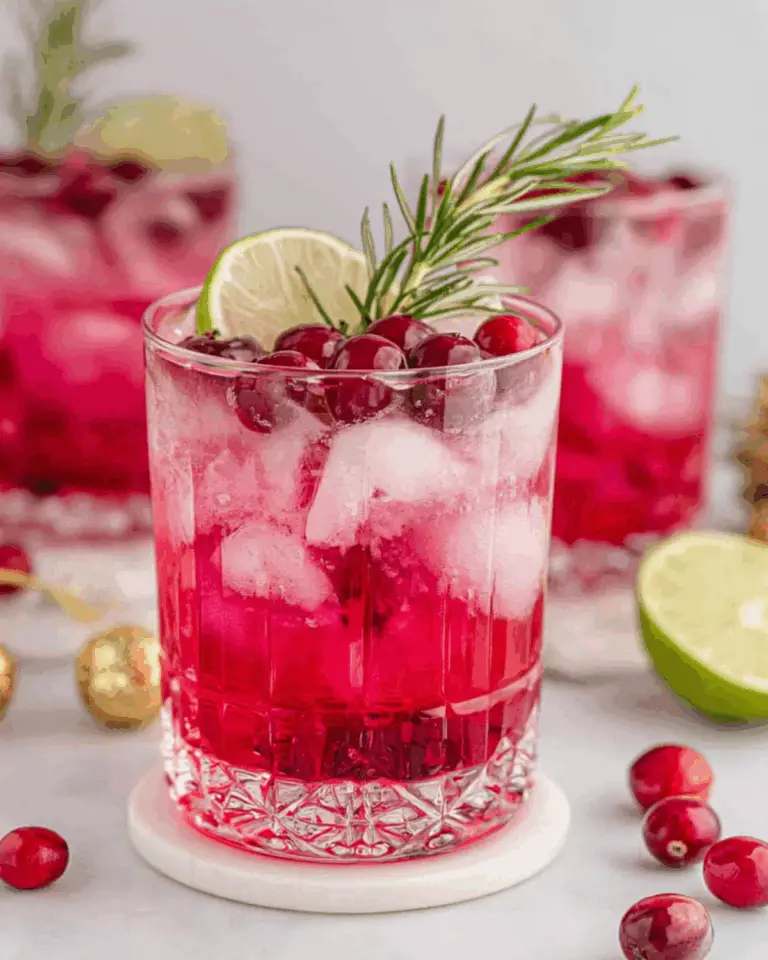 Cranberry Christmas Cocktail in a clear glass filled with ice, garnished with fresh cranberries, a lime slice, and a sprig of rosemary.