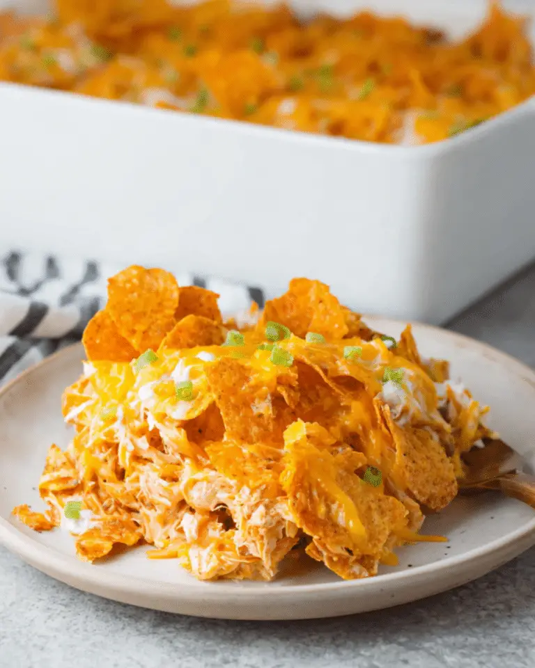 A serving of Doritos cheesy chicken casserole on a plate, topped with melted cheddar cheese and garnished with green onions.