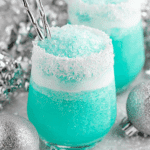 Vibrant blue Jack Frost cocktail in a glass rimmed with shredded coconut, topped with crushed ice, and surrounded by silver holiday decorations.
