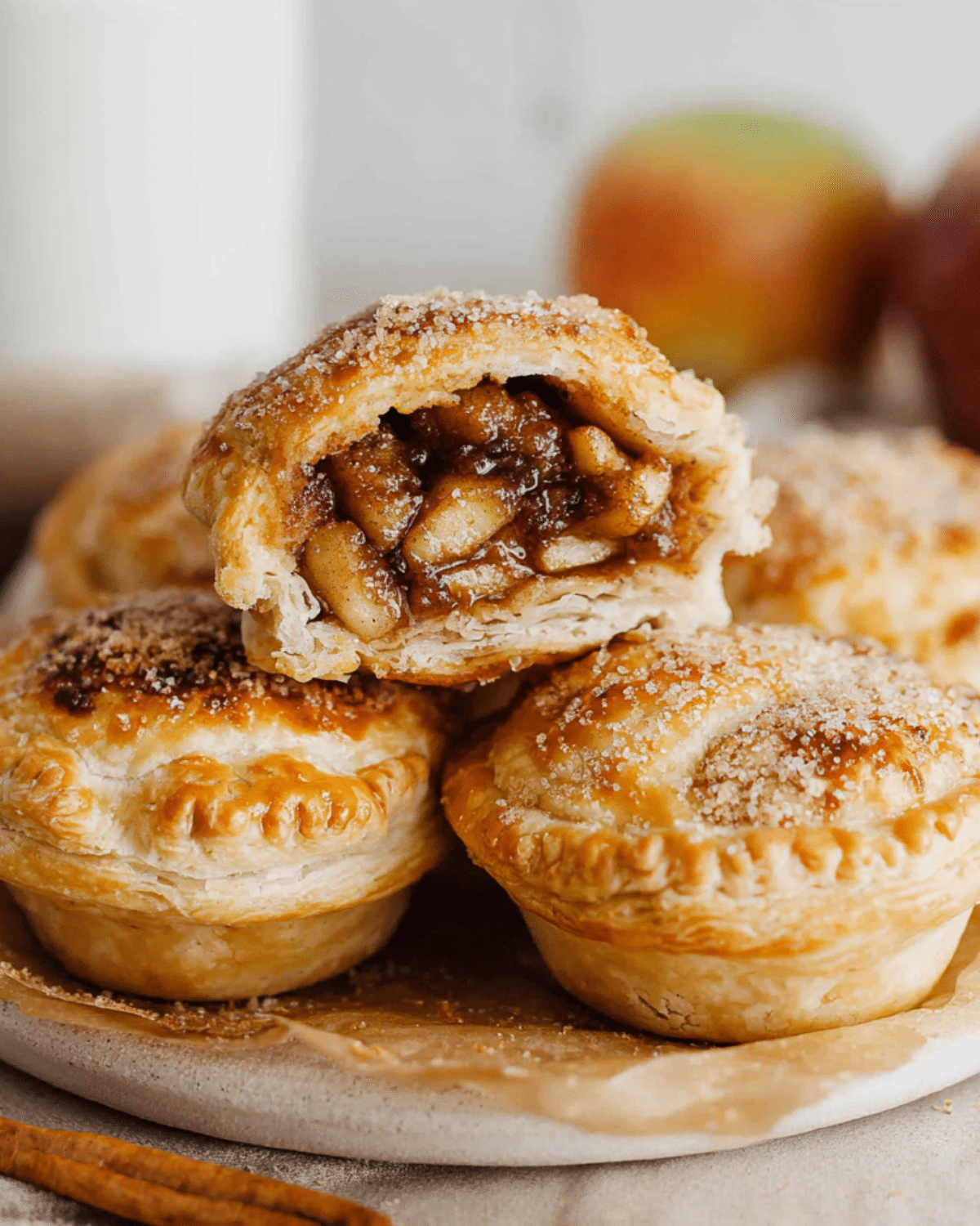 Golden Mini Apple Pies With Puff Pastry filled with spiced apple filling, stacked on a plate with one pie cut open to show the gooey interior.