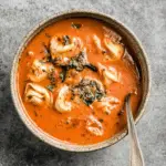 Bowl of pesto tomato tortellini soup filled with cheese tortellini, vibrant tomato broth, and topped with basil pesto.