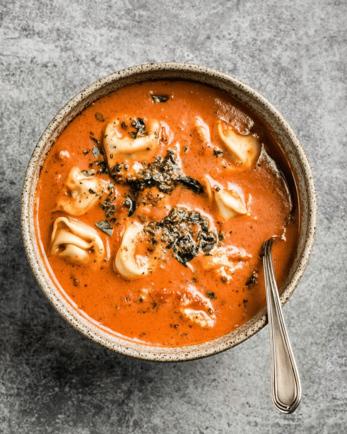 Bowl of pesto tomato tortellini soup filled with cheese tortellini, vibrant tomato broth, and topped with basil pesto.