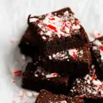 Stack of peppermint brownies topped with crushed candy canes on a white parchment background.