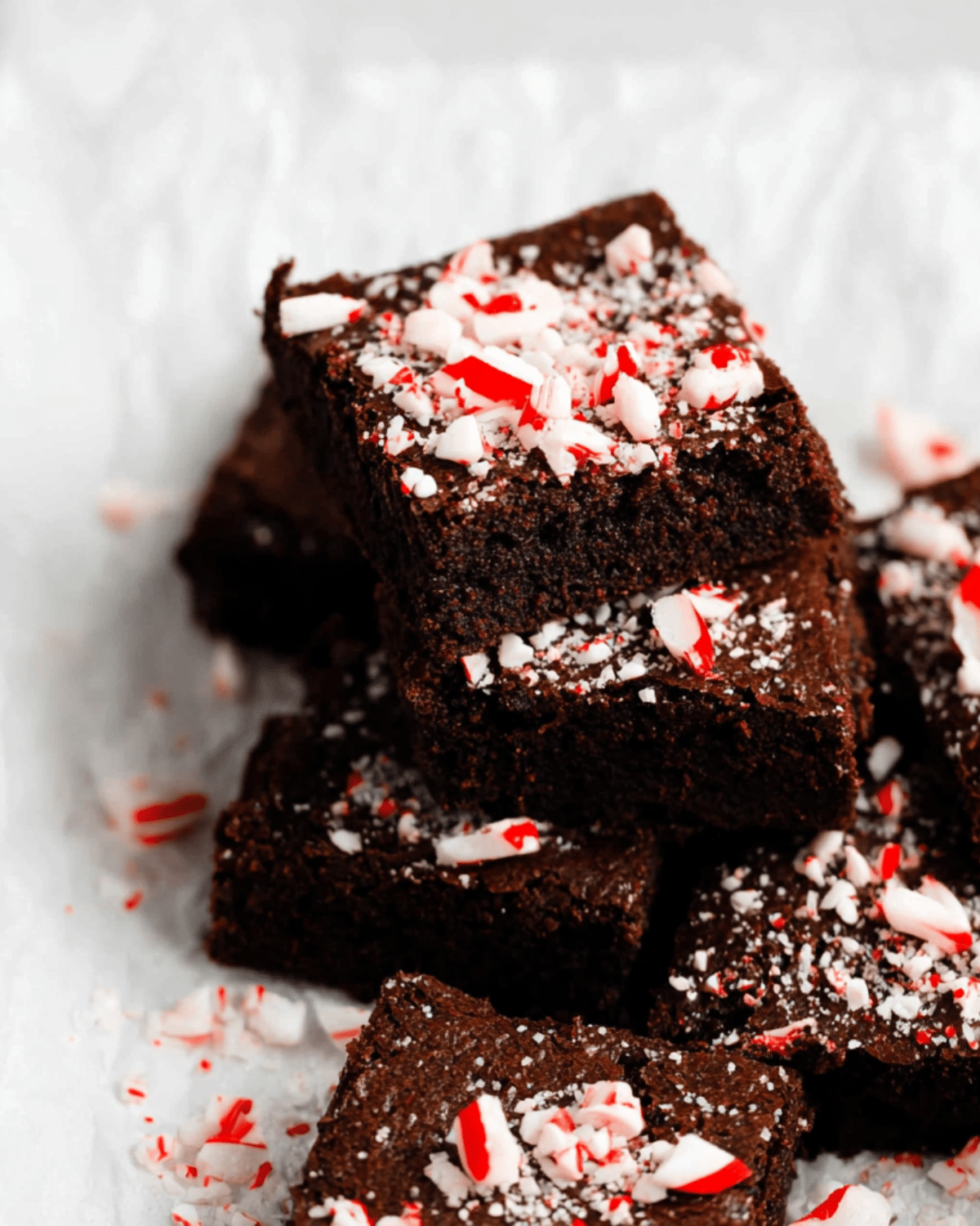 Stack of peppermint brownies topped with crushed candy canes on a white parchment background.