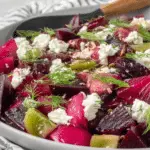 Close-up of Pickled Beet Salad with vibrant red and golden beets, crumbled goat cheese, fresh dill, and green tomato pieces on a white plate.