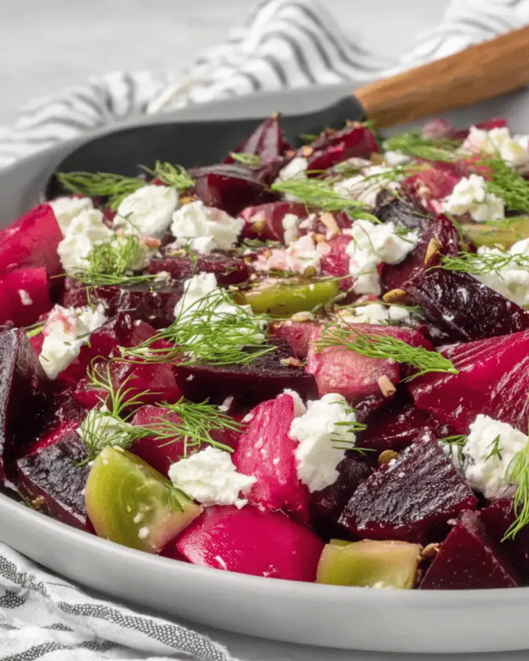 Close-up of Pickled Beet Salad with vibrant red and golden beets, crumbled goat cheese, fresh dill, and green tomato pieces on a white plate.