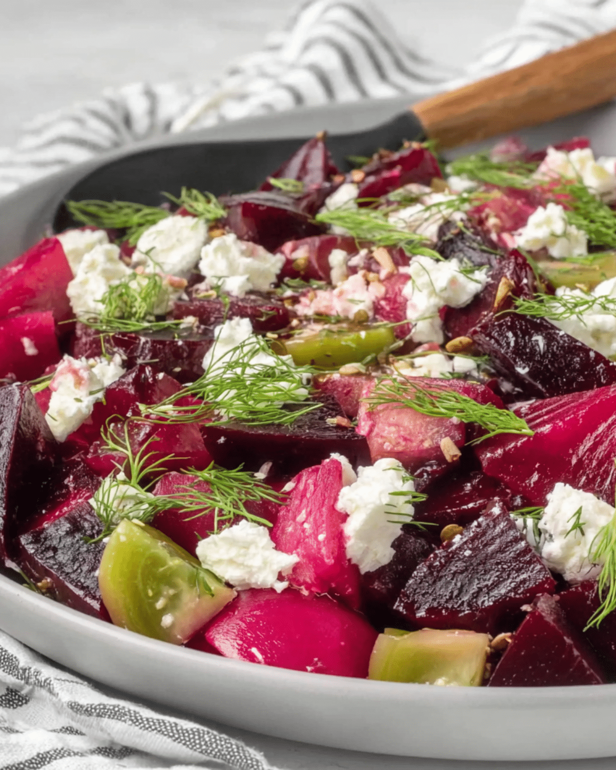 Close-up of Pickled Beet Salad with vibrant red and golden beets, crumbled goat cheese, fresh dill, and green tomato pieces on a white plate.