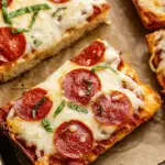 Close-up of cheesy pepperoni pizza bread slices topped with fresh basil on a baking sheet.