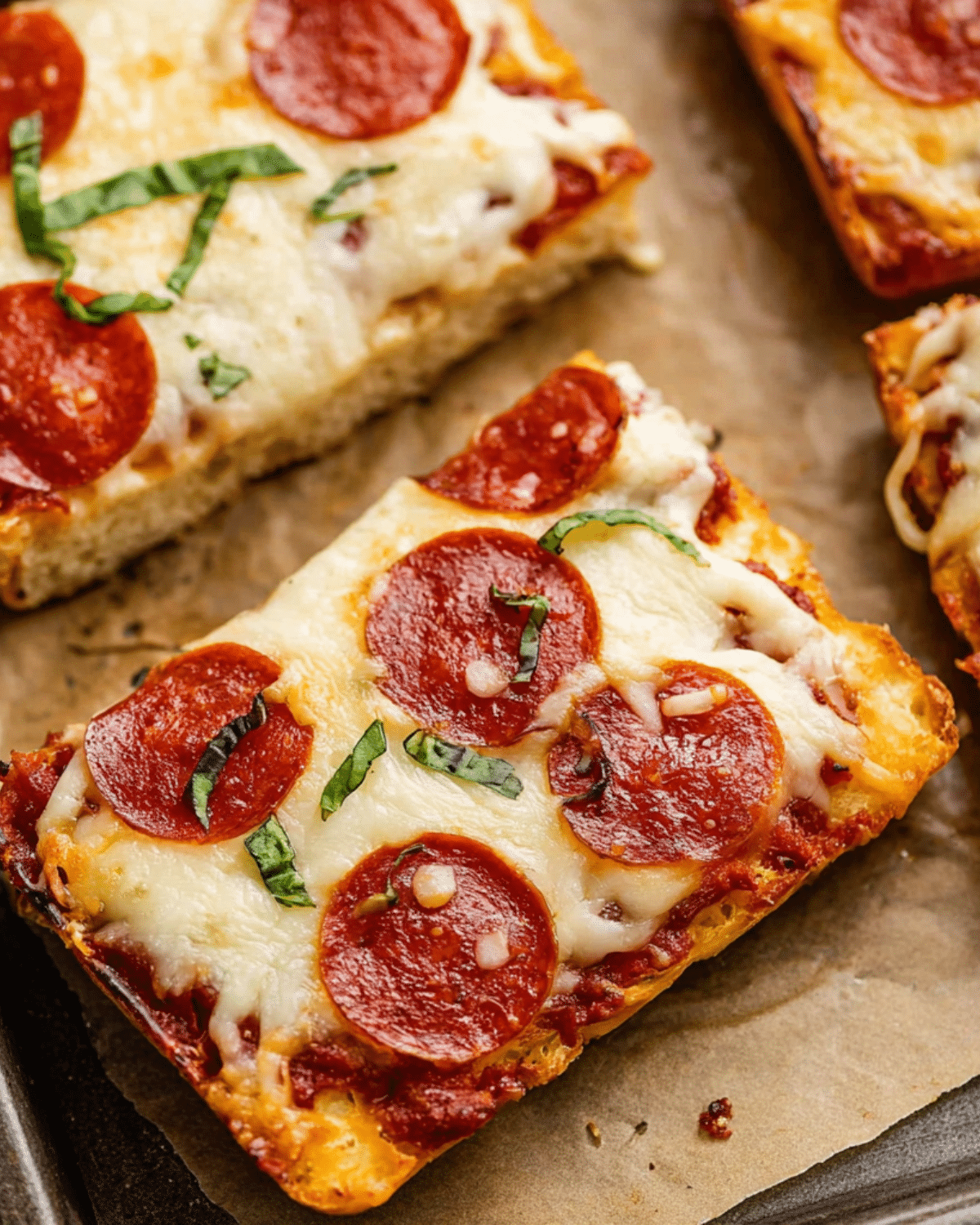 Close-up of cheesy pepperoni pizza bread slices topped with fresh basil on a baking sheet.