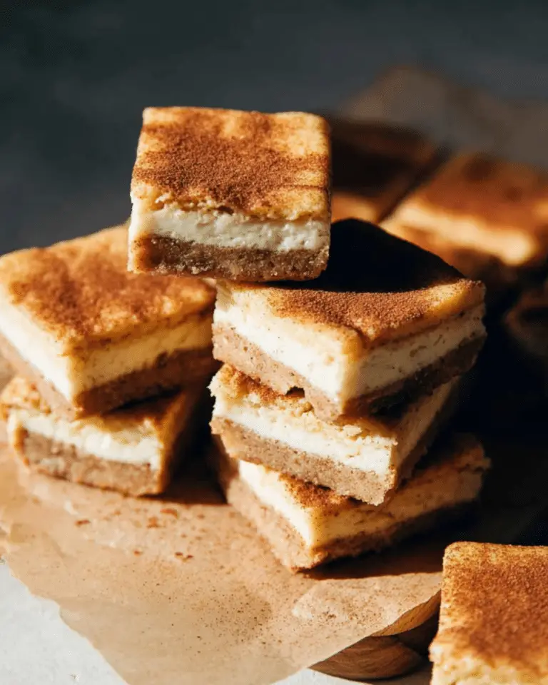 Stack of snickerdoodle cheesecake bars with cinnamon sugar topping, layered with creamy cheesecake and cookie crust.