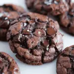 Close-up of triple chocolate cookies topped with flaky sea salt and loaded with melted chocolate chips.