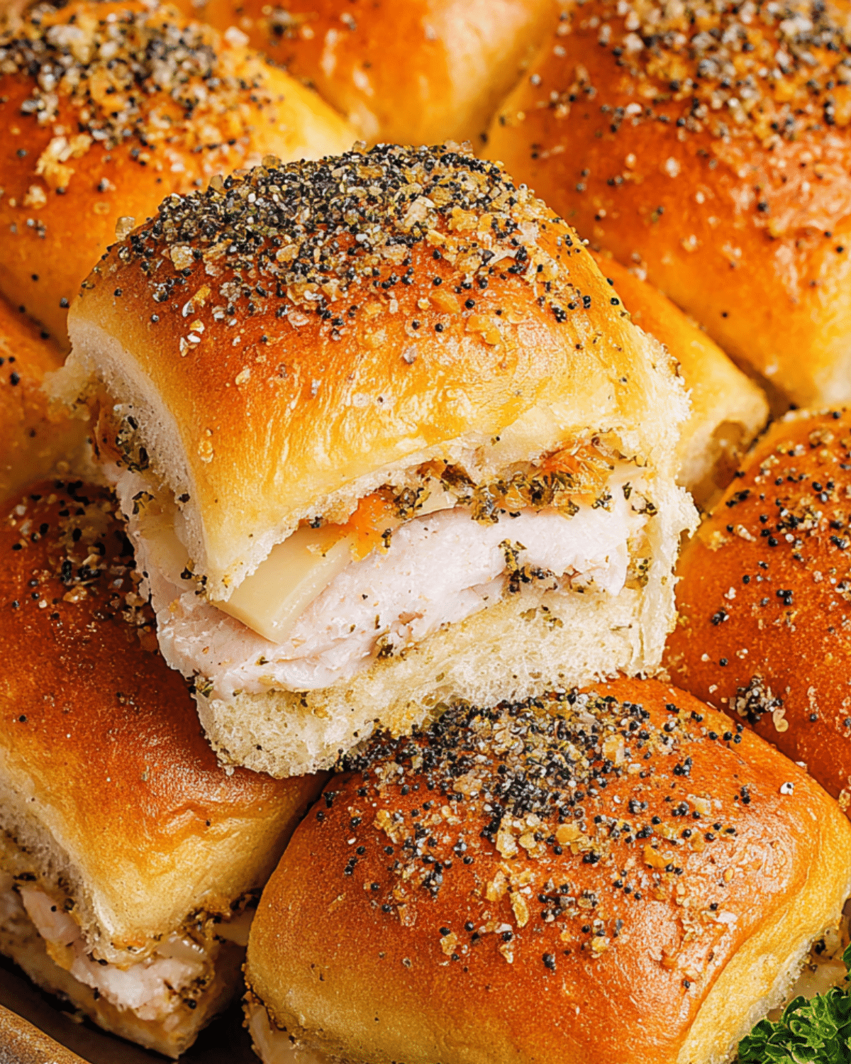 Close-up of freshly baked turkey sliders filled with sliced turkey and melted cheese, topped with a buttery poppy seed seasoning.