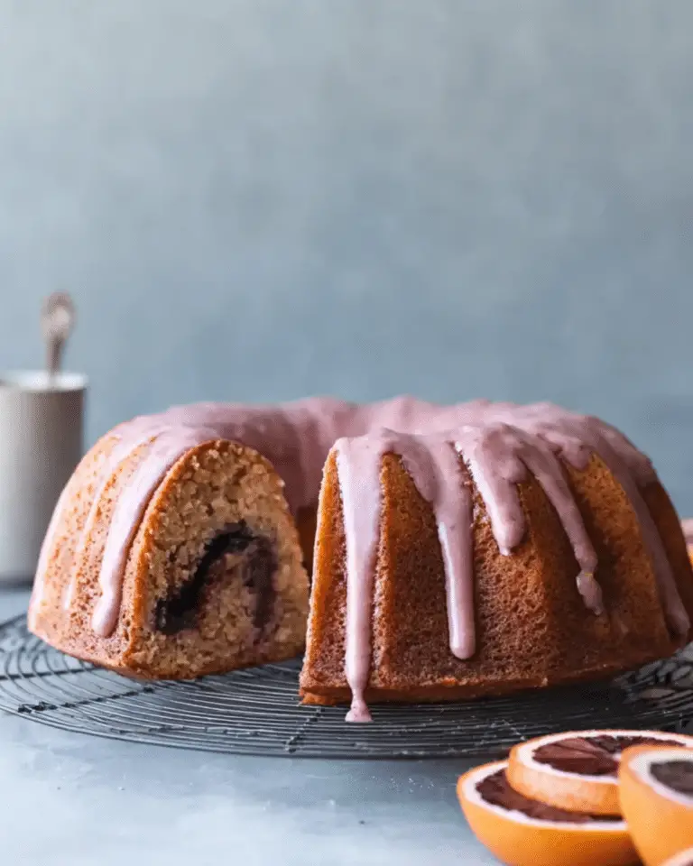 Blood orange coffee cake with a slice removed, revealing a swirl inside and topped with a pink blood orange glaze.