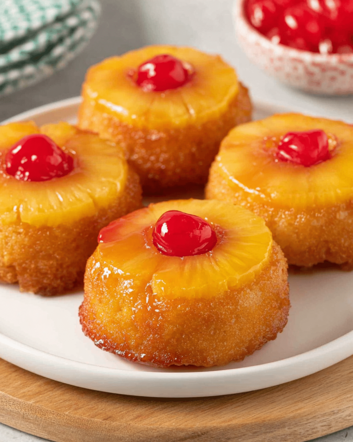 Mini pineapple upside down cakes topped with glazed pineapple rings and bright red maraschino cherries on a white plate.