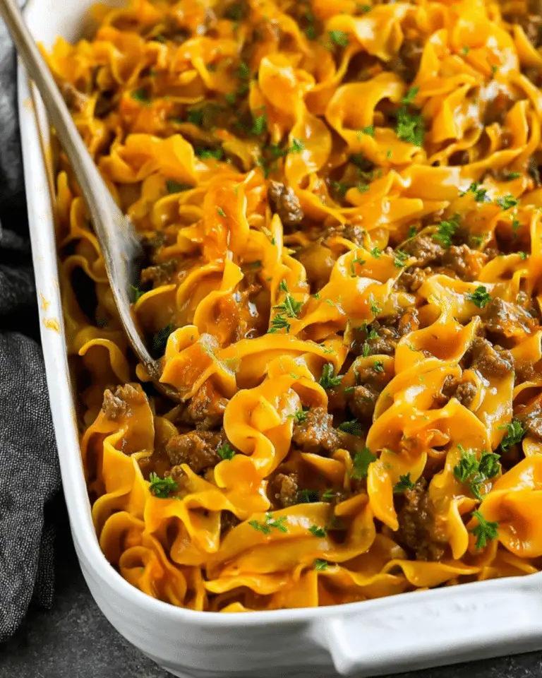 Close-up of a beef noodle casserole in a white baking dish, garnished with parsley.